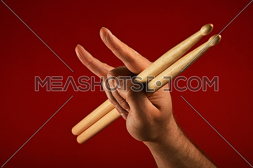 Man hand holding two drumsticks with devil horns rock metal gesture sign over red background, side view