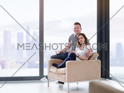 Young couple using tablet computer at luxury home together, looking at screen, smiling.