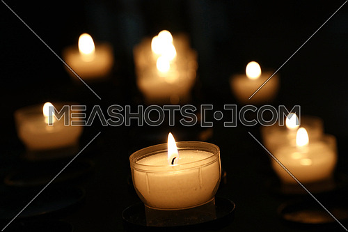 White translucent candles burning in dark church, close up, high angle view