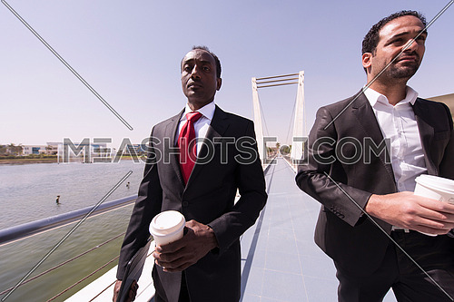 multi ethnic business people group walking across modern bridge while drinking first morning coffee