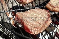 Raw beef bbq steaks cooking roasting on outdoors fire flame barbecue grill, one being turned with metal fork to another side, close up