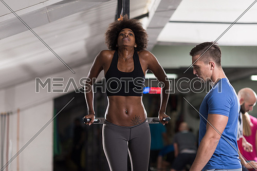 african american athlete woman workout out arms on dips horizontal parallel bars Exercise training triceps and biceps doing push ups with trainer