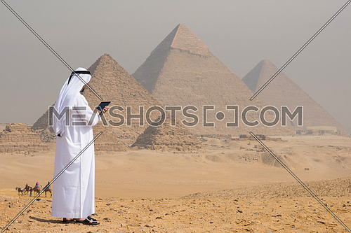 arabian business man using tablet computer in desert with great giza pyramids in background