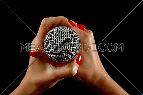 Woman holding microphone with two hands with red nails isolated on black background