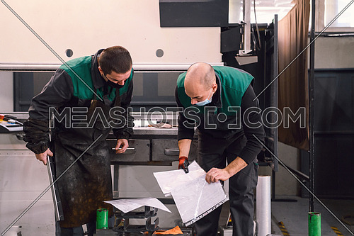 two workers wearing a protective mask due to a coronavirus pandemic, working in a modern factory, and preparing a program and material for a CNC machine. High quality photo
