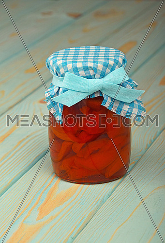 One glass jar of homemade quince jam with textile top decoration at blue painted vintage wooden surface