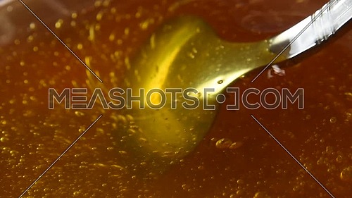 Close up spinning metal spoon in bowl of fresh thick fluid acacia honey, high angle view, slow motion