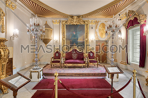 Cairo, Egypt - October 21, 2017: Throne Hall at Manial Palace of Prince Mohammed Ali Tewfik with gold plated red armchairs, antique floor lamps, ornate ceiling and red carpets