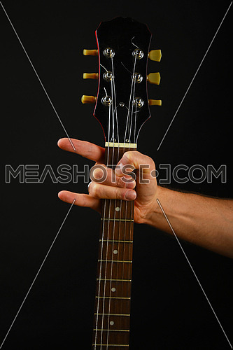 Male hand holding guitar neck with devil horns rock metal sign isolated on black background