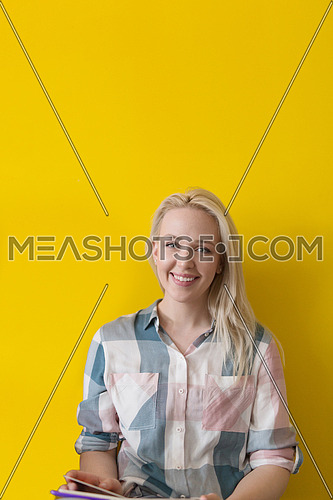 Young casual woman sitting on floor and reading a book, isolated on yellow background