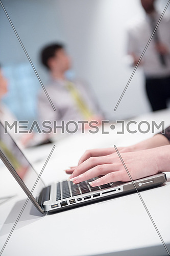 business woman hands typing on laptop  computer  on meeting, blurred people group brainstorming in background  at modern bright office interior