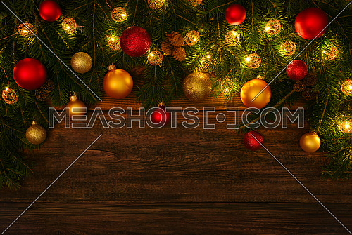 Close up fresh green spruce or pine Christmas tree branches with cones, lights, colorful balls and baubles decoration, over dark brown wooden planks background with copy space