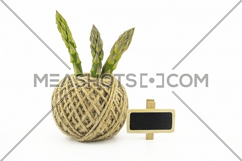 Fresh green asparagus spears and ball of natural hemp twine alongside a small slate or signboard isolated on white background, selective focus in a low angle view