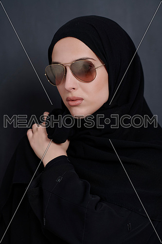 Young muslim businesswoman in traditional clothes or abaya and sunglasses posing in front of black chalkboard. Arab woman representing modern arabic lifestyle, islamic  fashion and Ramadan kareem concept