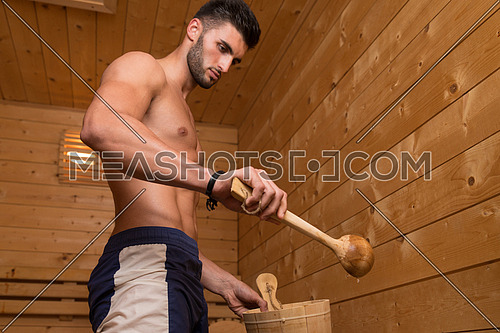Happy Good Looking And Attractive Young Man With Muscular Body Pouring Water On Hot Rocks In Sauna
