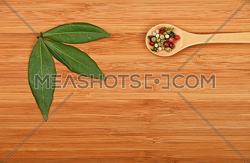 Group of three bay laurel leaves and mix of peppercorn in wooden spoon on bamboo wood chopping board background