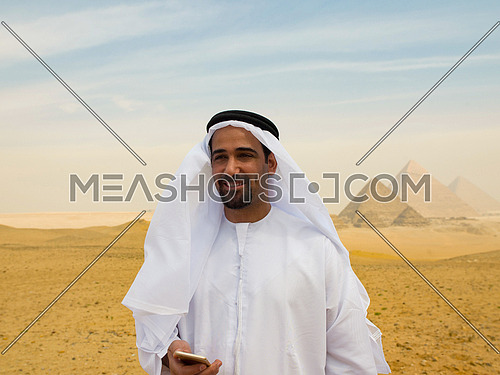 young man as tourist  wearing  arabian traditional clothes in egypt with giza pyramids in background  using smartphone