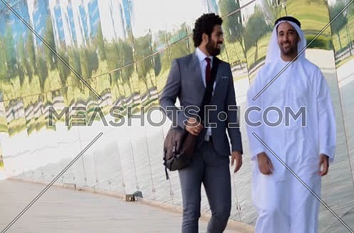 Two business men one wearing traditional emirati thob walking discussing