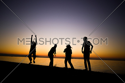 Four friends standing and jumping and having fun at the beach enjoying the golden hour by sunset golden hour
