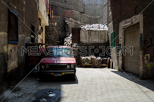 An old red car parked in an empty alley in Cairo at day