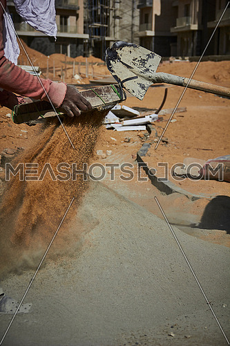 Mid Shot for worker sifting Cement in a construction site at day