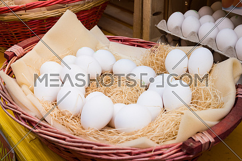 White chicken eggs leaning on straw in wooden basket at market,outdoor.