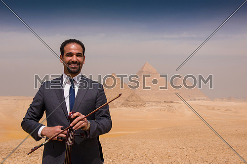 chello player in egyptian desert with pyramids in background