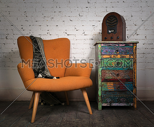 Composition of vintage orange armchair, colorful cupboard and aged wooden radio