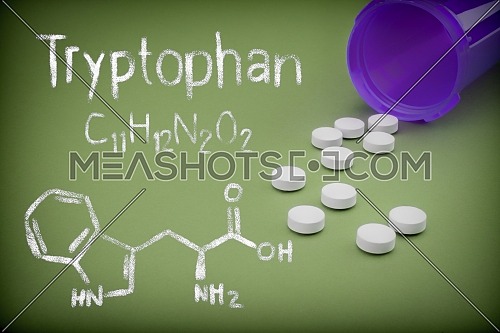 Pills spilling from an open bottle on green background, Chemical formulation of trytophan written with chalk, conceptual image