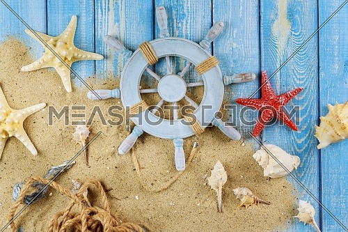 Decorative steering wheel with starfish, seashells on the sandy beach old blue wood background