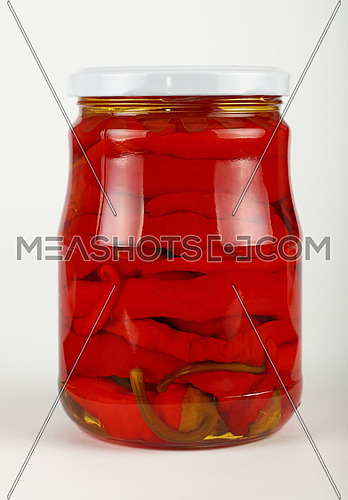 Close up of one glass jar of pickled red hot cherry chili pepperoncini peppers over white background, low angle side view