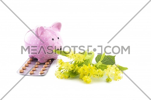 Conceptual of the cost of healthcare and medicine with ceramic piggy bank tablets and freshly picked yellow linden flowers over a white background