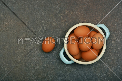 Close up pan bowl of brown chicken eggs on dark grunge table surface, elevated top view, directly above