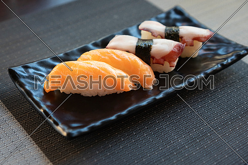 Traditional japanese nigiri sushi with salmon and sushi with octopus on black plate.