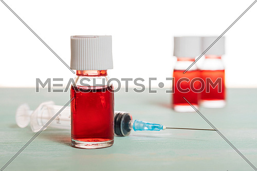 medical vaccine phials with red liquid and syringe over green table and white background. Vaccination and immunization conceptual.