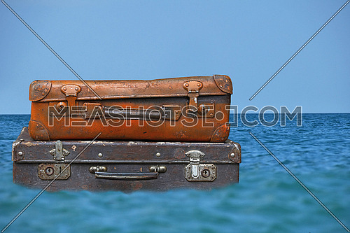 Stack of two old vintage antique grunge travel luggage brown leather suitcase trunks floating in blue sea water under clear sky, close up, low angle side view