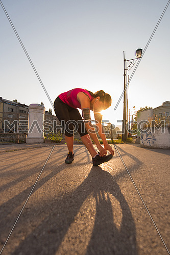 athlete woman warming up and stretching while preparing for running on the city street at  sunny morning