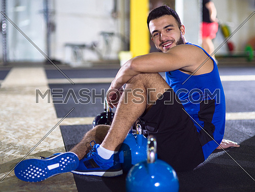 young athlete man sitting on the floor and relaxing before a hard training at crossfitness gym