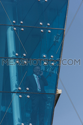 Outdoor shoot of a senior executive talking on the phone through glass front of a  corporate building with blue sky at the background