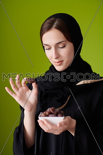 Modern Muslim Woman in Abaya Holding a Date Fruit and glass of water in from of her. Concept celebration of iftar in ramadan and end of feasting