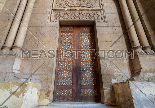External old decorated bricks stone wall with arabesque decorated wooden door framed by stone ornate cylindrical columns leading to al Rifai Mosque, Old Cairo, Egypt