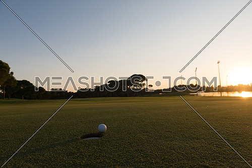 golf ball on edge of course hole representing achivement and success business concept, beautiful sunset in background