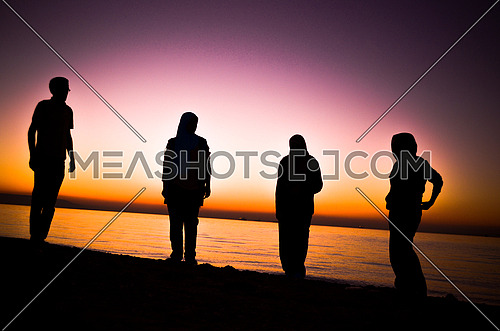 a group of four friends standing by the beach at sunset