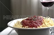 hand putting spaghetti with minced beef plate on table and pouring wine in glass