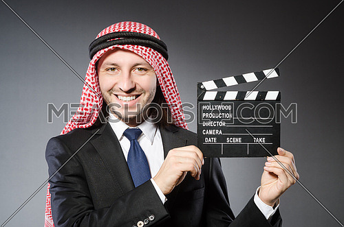 Arab man with movie clapper against grey background