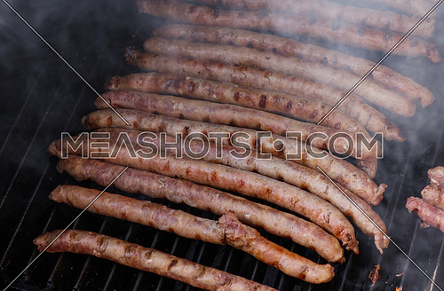 Close up cooking meat sausages on grill, smoking and broiling them, high angle view