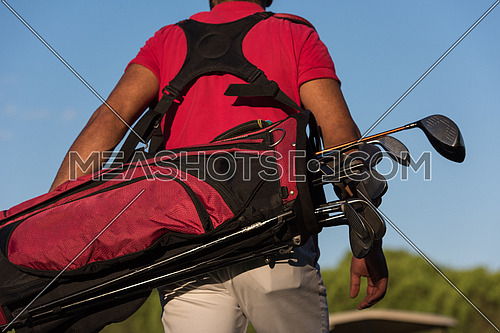 close up of golfers back while carrying  golf bag  and walking at course to next hole