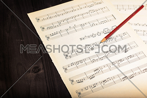 In the picture aged pages of sheet music, pencil  and wooden background,used split tonig for old/vintage style.