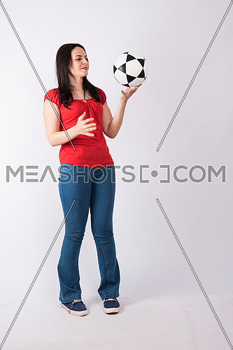 young lady standing and playing with a ball on white background wearing red shirt and jeans