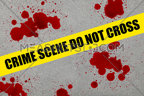 Close up yellow police barricade tape with crime scene do not cross words over blood stains splattered on grey stone floor background
